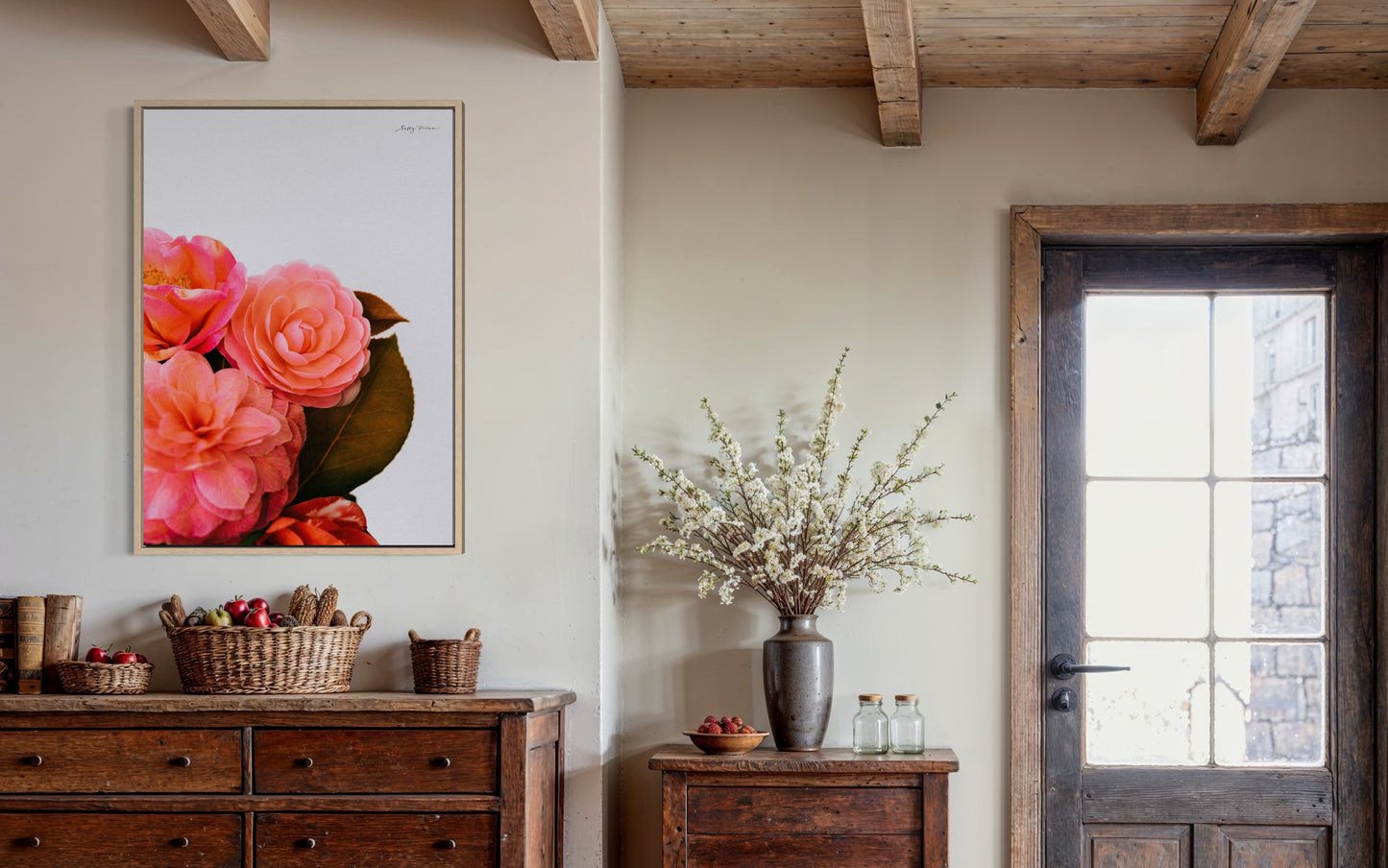 A photographic fine art print of a bright pink bunch of flowers on a white background. The flowers include camellias and the print is framed in a natural wood colour. The frames art is hung in a rustic looking home with modern wooden features. 