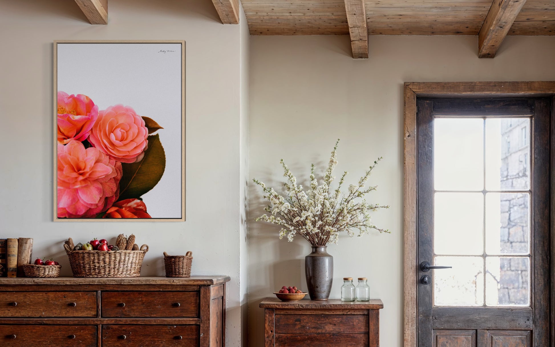 A photographic fine art print of a bright pink bunch of flowers on a white background. The flowers include camellias and the print is framed in a natural wood colour. The frames art is hung in a rustic looking home with modern wooden features. 