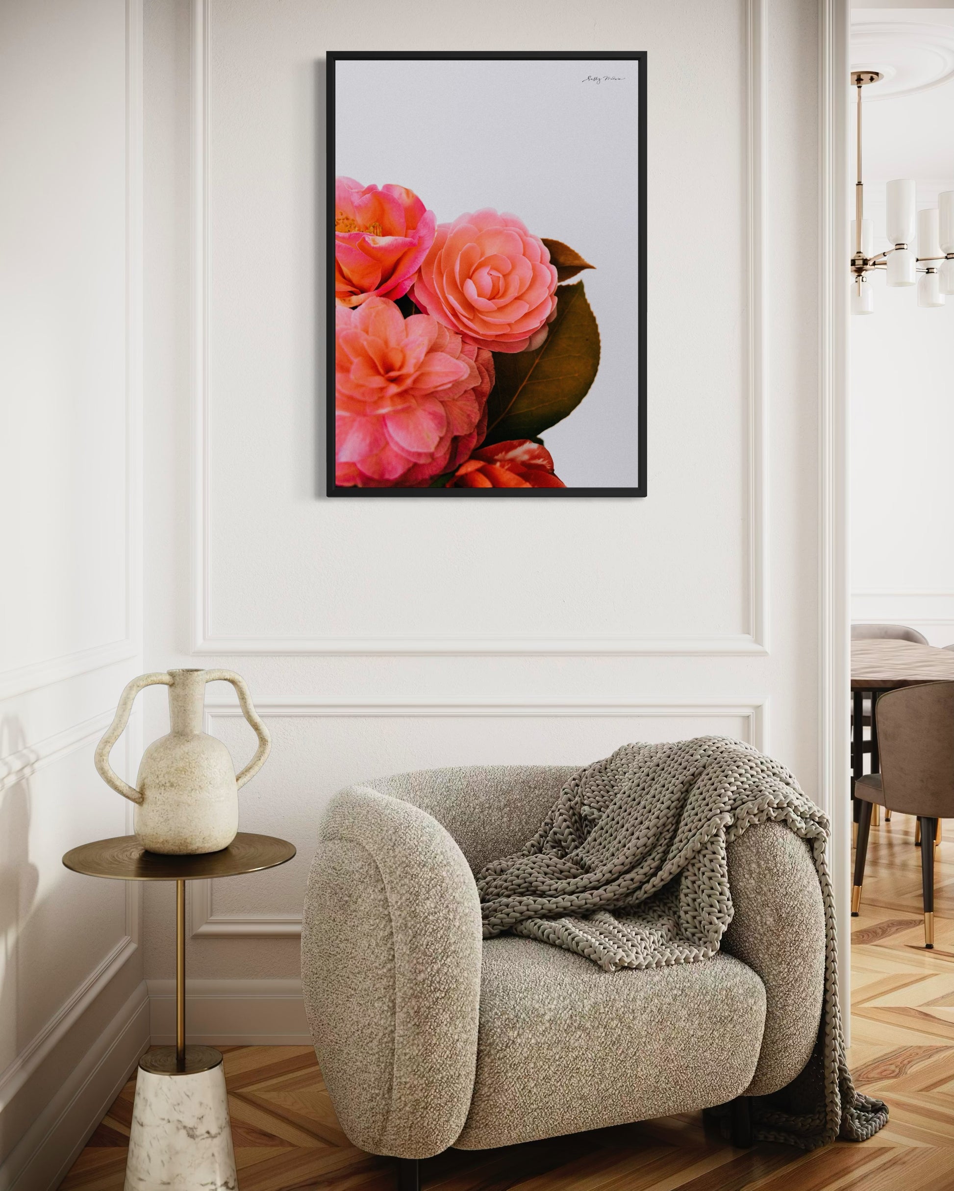 A photographic fine art print of a bright pink bunch of flowers on a white background. The flowers include camellias and the print is framed in a black wood. The print is hung on a white wall in a modern renovation of a 1930s home 