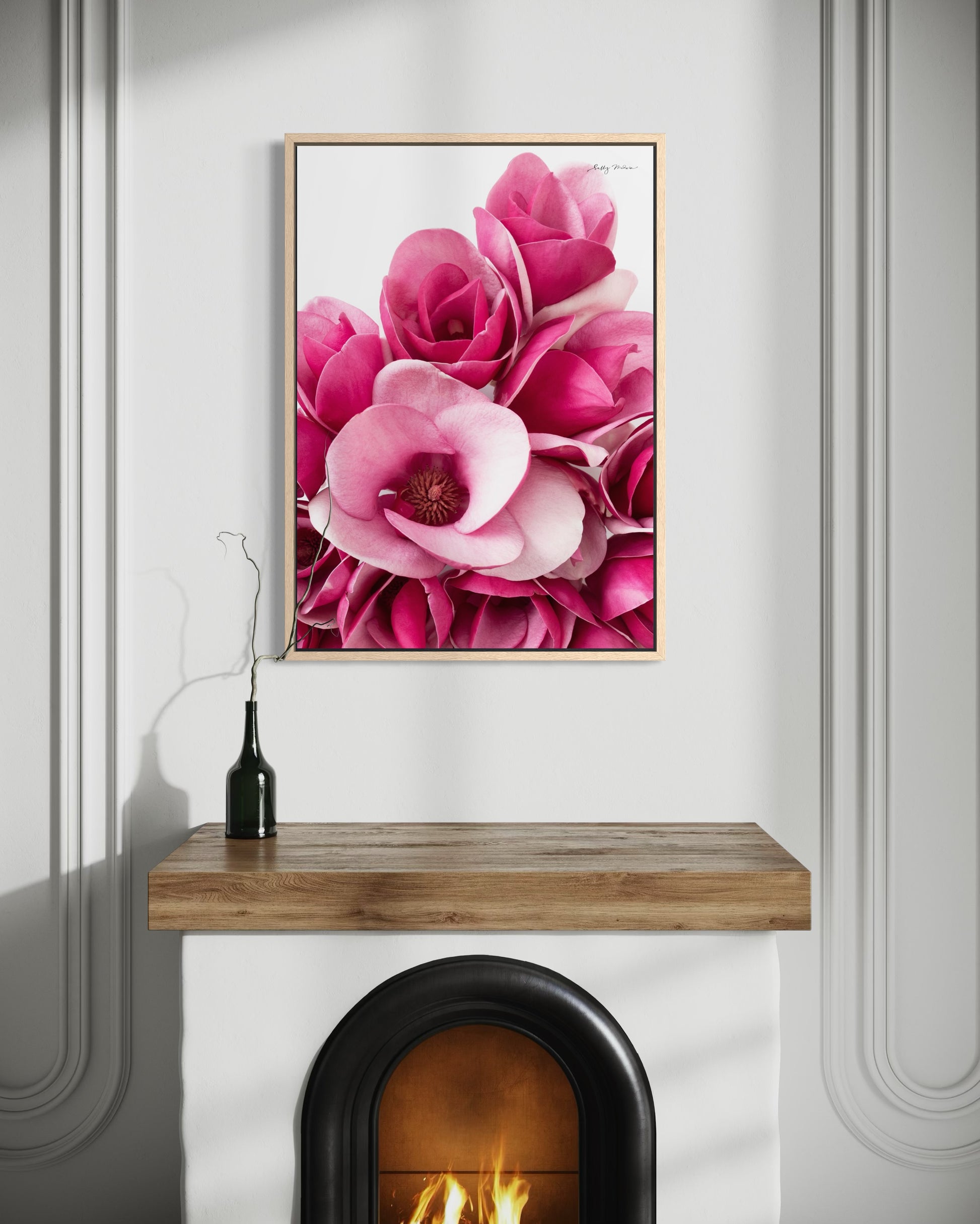 A photographic fine art print of a bunch of pink magnolia flowers. The art is framed and set above a fireplace 