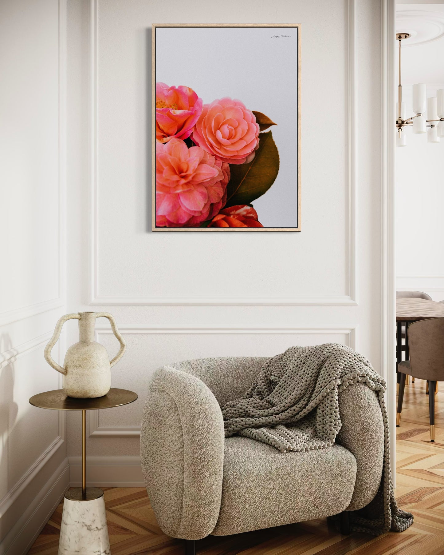 A photographic fine art print of a bright pink bunch of flowers on a white background. The flowers include camellias and the print is framed in a natural wood colour. The print is hung on a white wall in a modern renovation of a 1930s home 