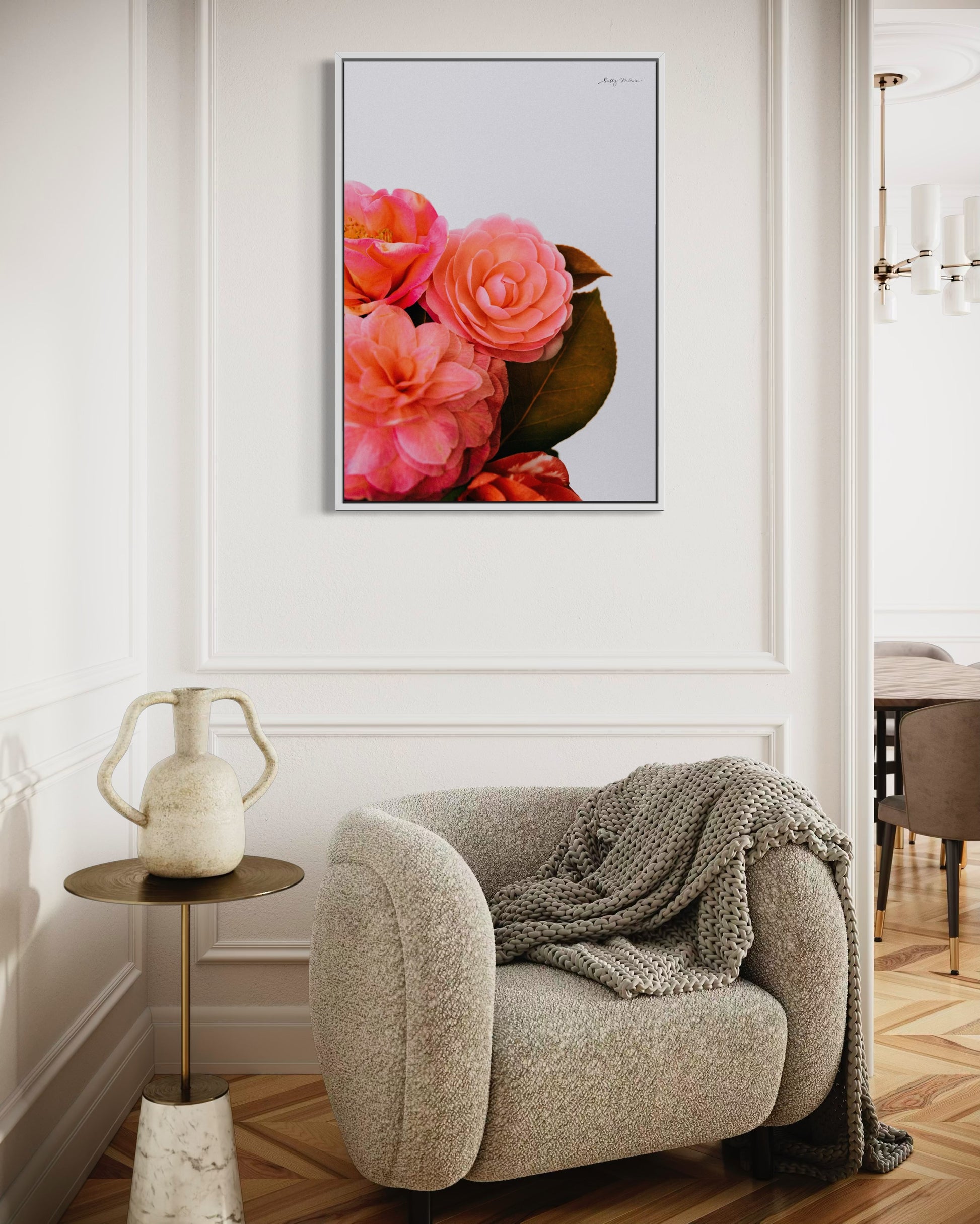 A photographic fine art print of a bright pink bunch of flowers on a white background. The flowers include camellias and the print is framed in a white wood colour. The print is hung on a white wall in a modern renovation of a 1930s home 