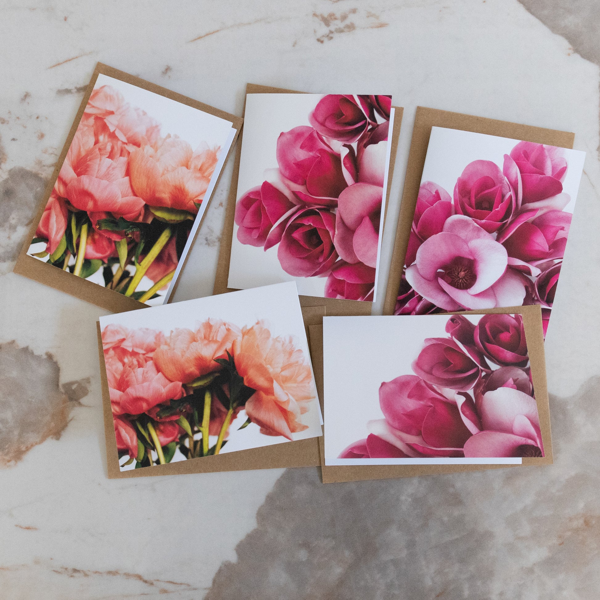 Set of five cards with original colourful fine art photography prints of peony and magnolia flowers laid flat on a marble surface.