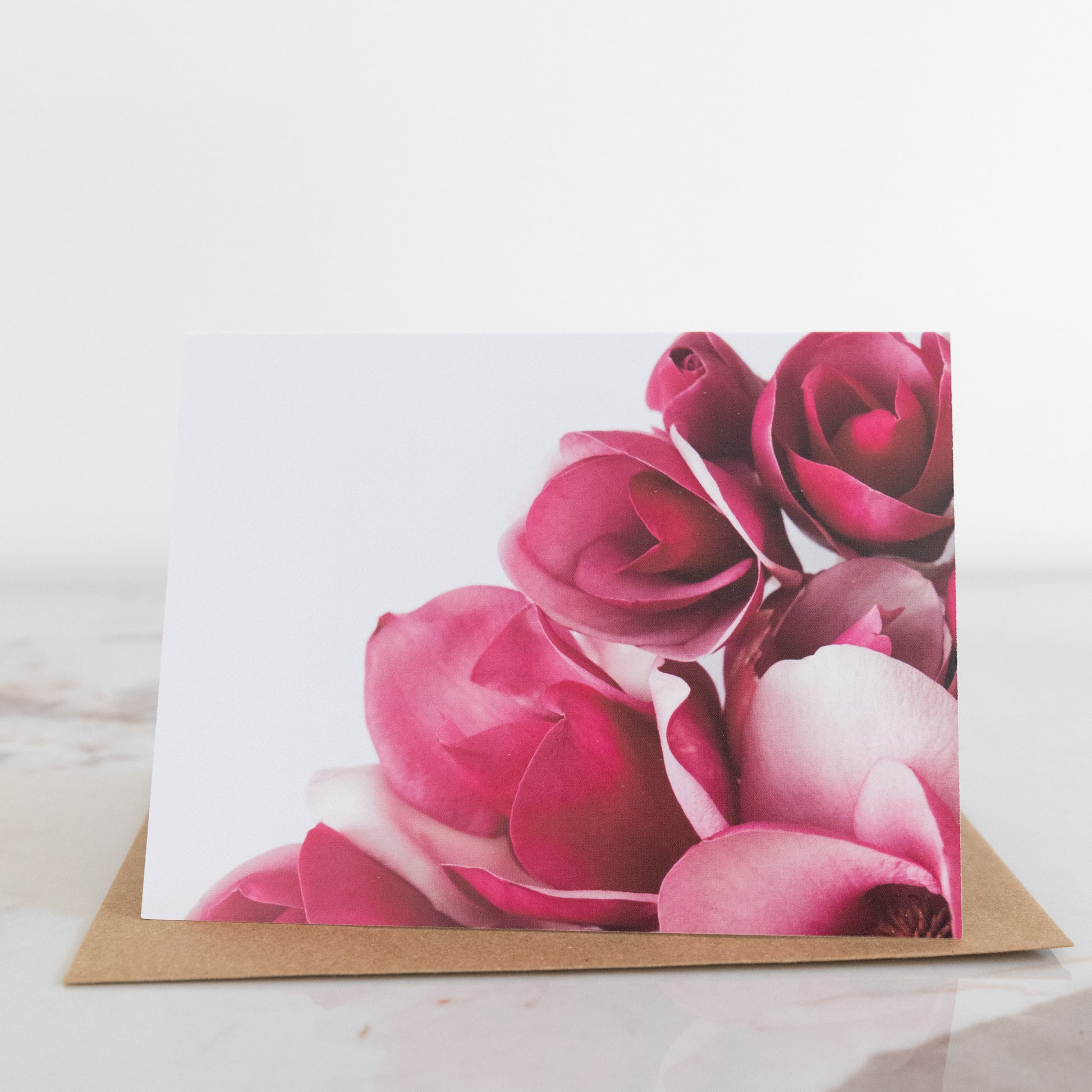 A magnolia flower fine art photography print greeting card, sat up on a marble and white background. It has a brown envelope.