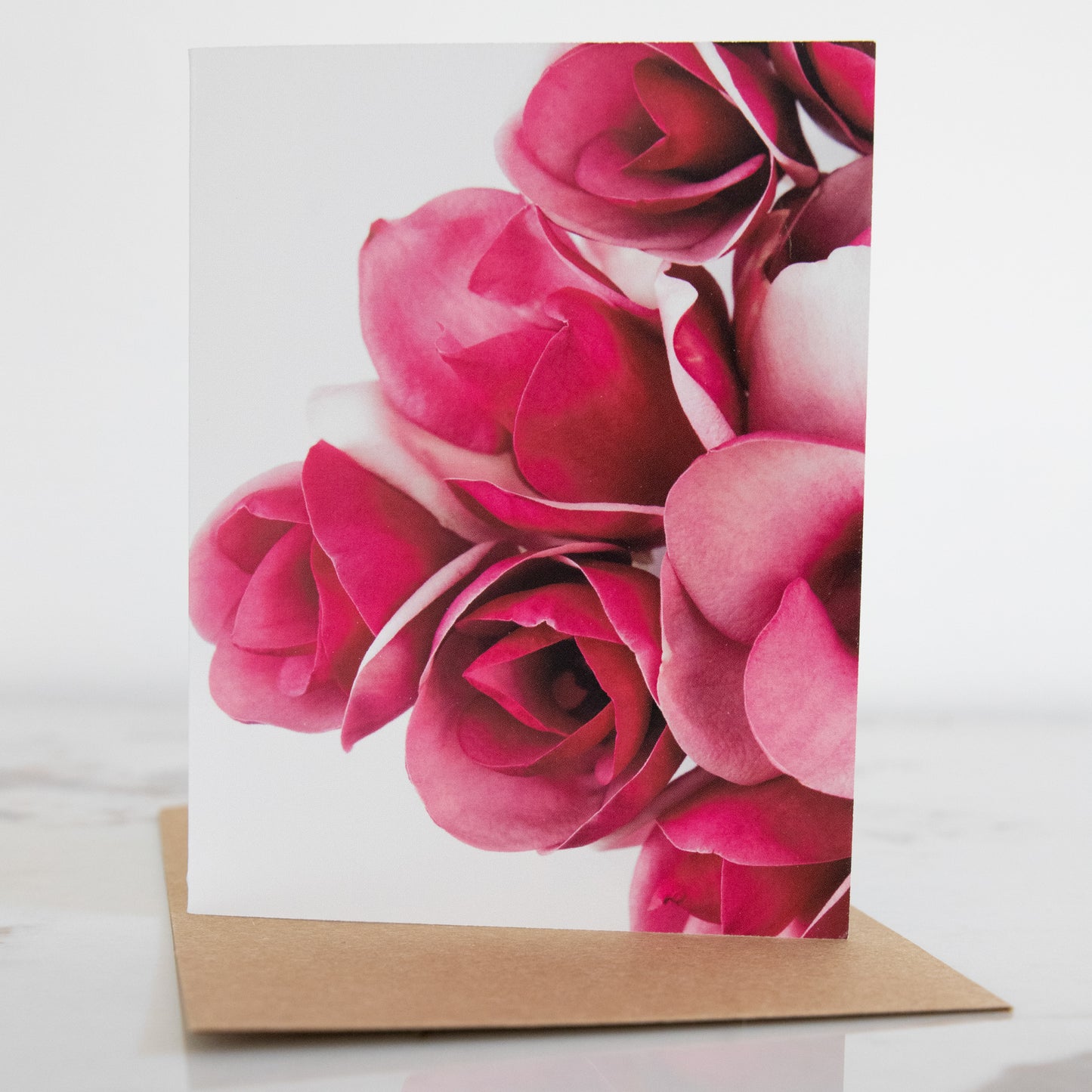 A magnolia flower fine art photography print greeting card, sat up on a marble and white background. It has a brown envelope.This is a greeting card in portrait aspect. 