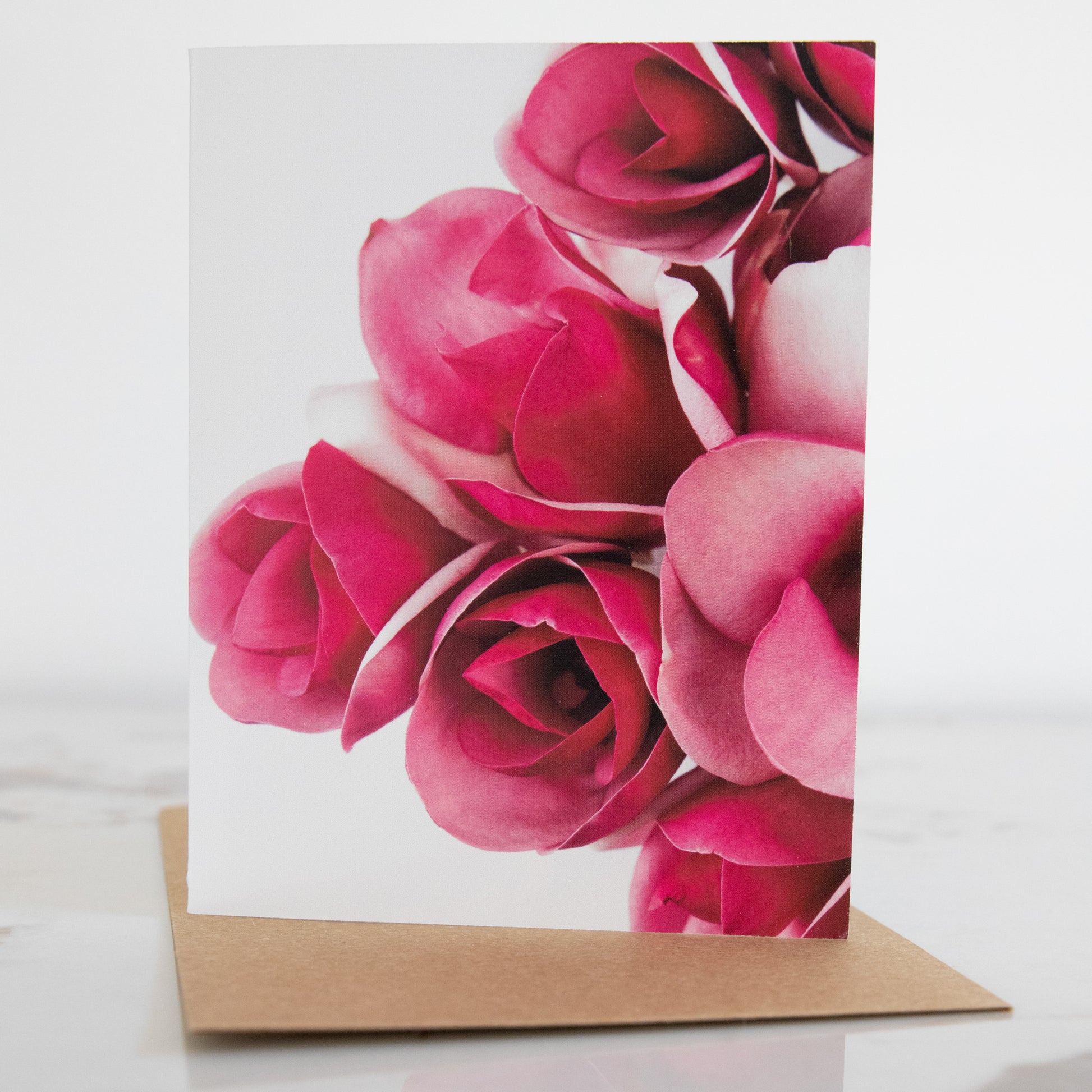 A magnolia flower fine art photography print greeting card, sat up on a marble and white background. It has a brown envelope.This is a greeting card in portrait aspect. 