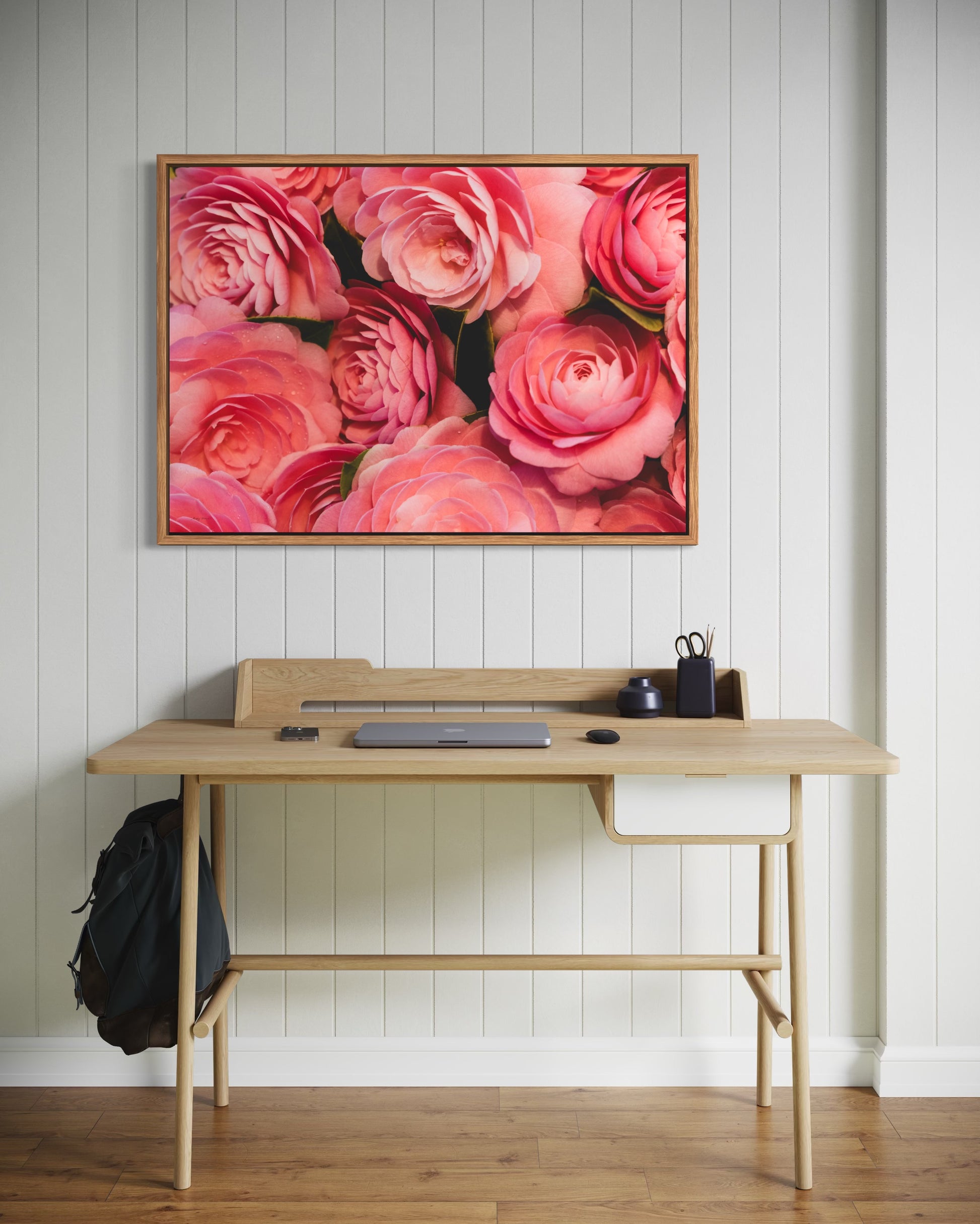 Wooden desk with a floral photography print on the wall in a room with wooden flooring.